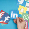 Hand holding social media icons, including LinkedIn, Facebook, Twitter, and WhatsApp, symbolizing social media marketing strategies for life coaches.