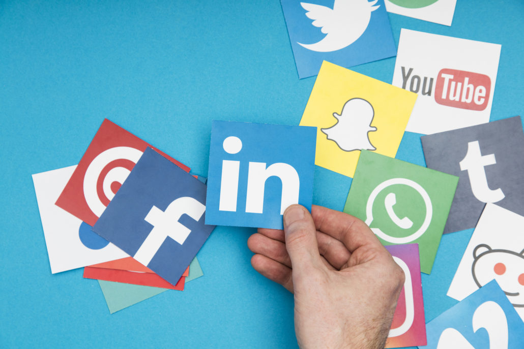 Hand holding social media icons, including LinkedIn, Facebook, Twitter, and WhatsApp, symbolizing social media marketing strategies for life coaches.