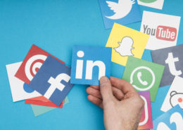 Hand holding social media icons, including LinkedIn, Facebook, Twitter, and WhatsApp, symbolizing social media marketing strategies for life coaches.