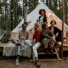 A diverse group of young adults sitting together in front of a glamping tent in the forest, symbolizing connection, reflection, and community at a life coaching retreat.