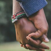 Relationship Coaching Certification: Building Stronger Connections – A close-up of two people holding hands, symbolizing trust, support, and emotional connection. One person wears a beaded bracelet with vibrant colors, adding a touch of cultural significance. The blurred background suggests an outdoor setting, emphasizing warmth and togetherness.