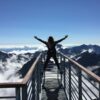 Person standing with arms wide open on a mountain viewpoint above the clouds, symbolizing freedom, possibility, and The Power of AND™.