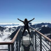 Person standing with arms wide open on a mountain viewpoint above the clouds, symbolizing freedom, possibility, and The Power of AND™.