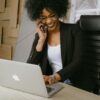 Smiling woman sitting in front of a laptop, talking on her phone, celebrating progress—symbolizing how to help a stuck client move forward.
