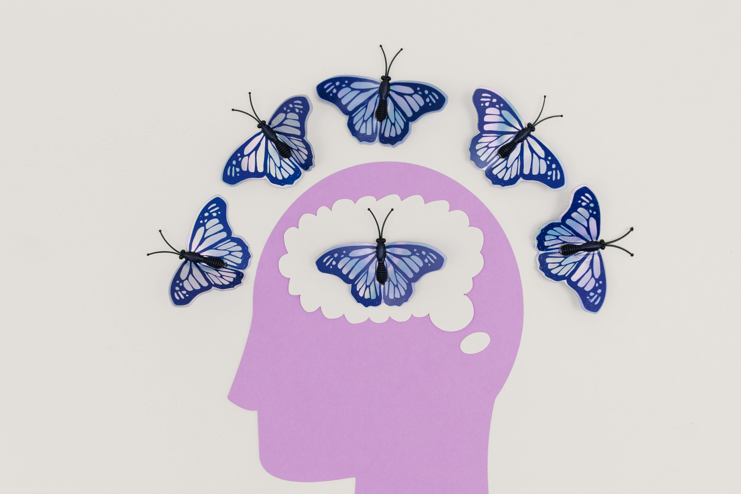 Creative coaching with art therapy concept showing blue butterflies emerging from a paper-cut human mind, symbolizing emotional expression and personal transformation.