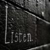 Word 'Listen' written on a dark brick wall, symbolizing the power of active listening in coaching to build trust and transformation.