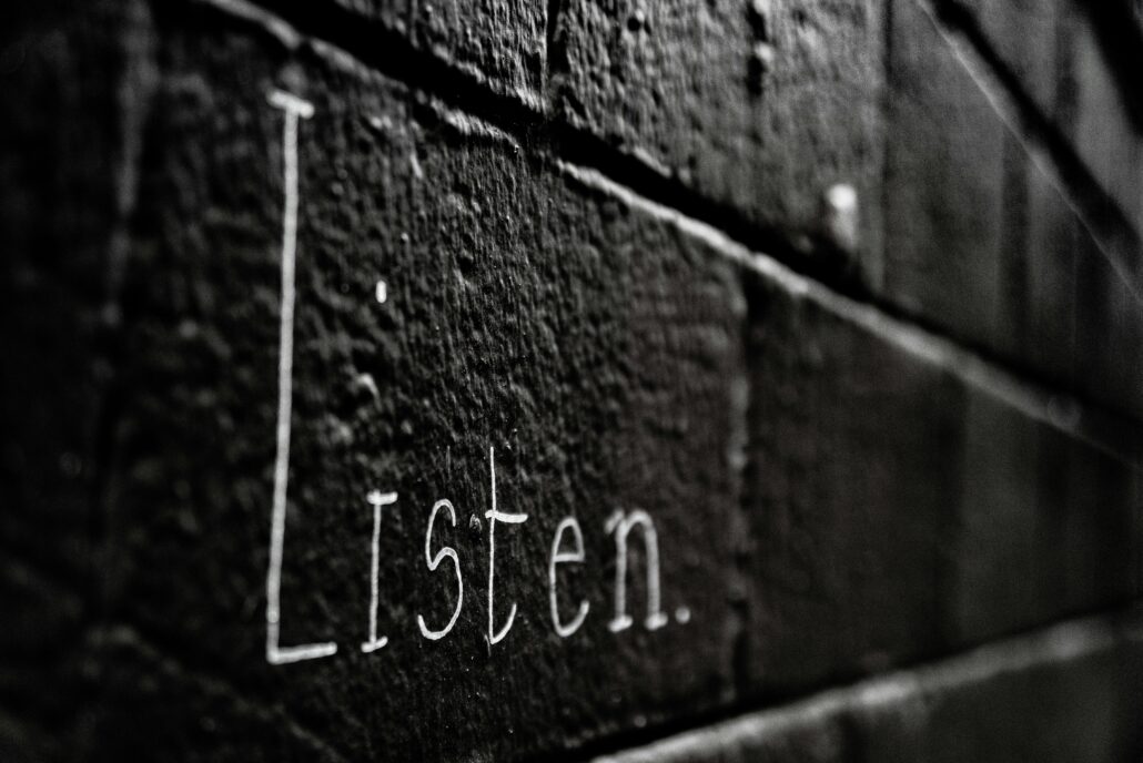 Word 'Listen' written on a dark brick wall, symbolizing the power of active listening in coaching to build trust and transformation.