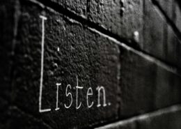 Word 'Listen' written on a dark brick wall, symbolizing the power of active listening in coaching to build trust and transformation.